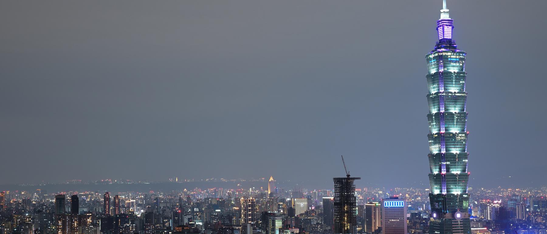 Night skyline of Taipei with high-rise office towers seen from a forested mountain trail