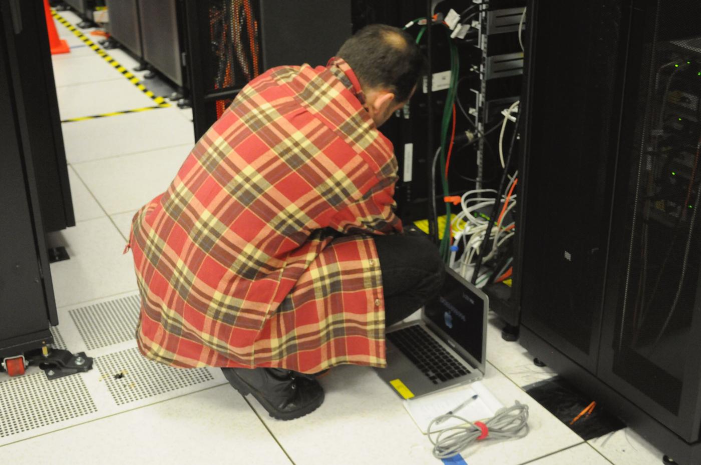 A technician with a laptop checking cable connections inside an open server rack in a computing centre